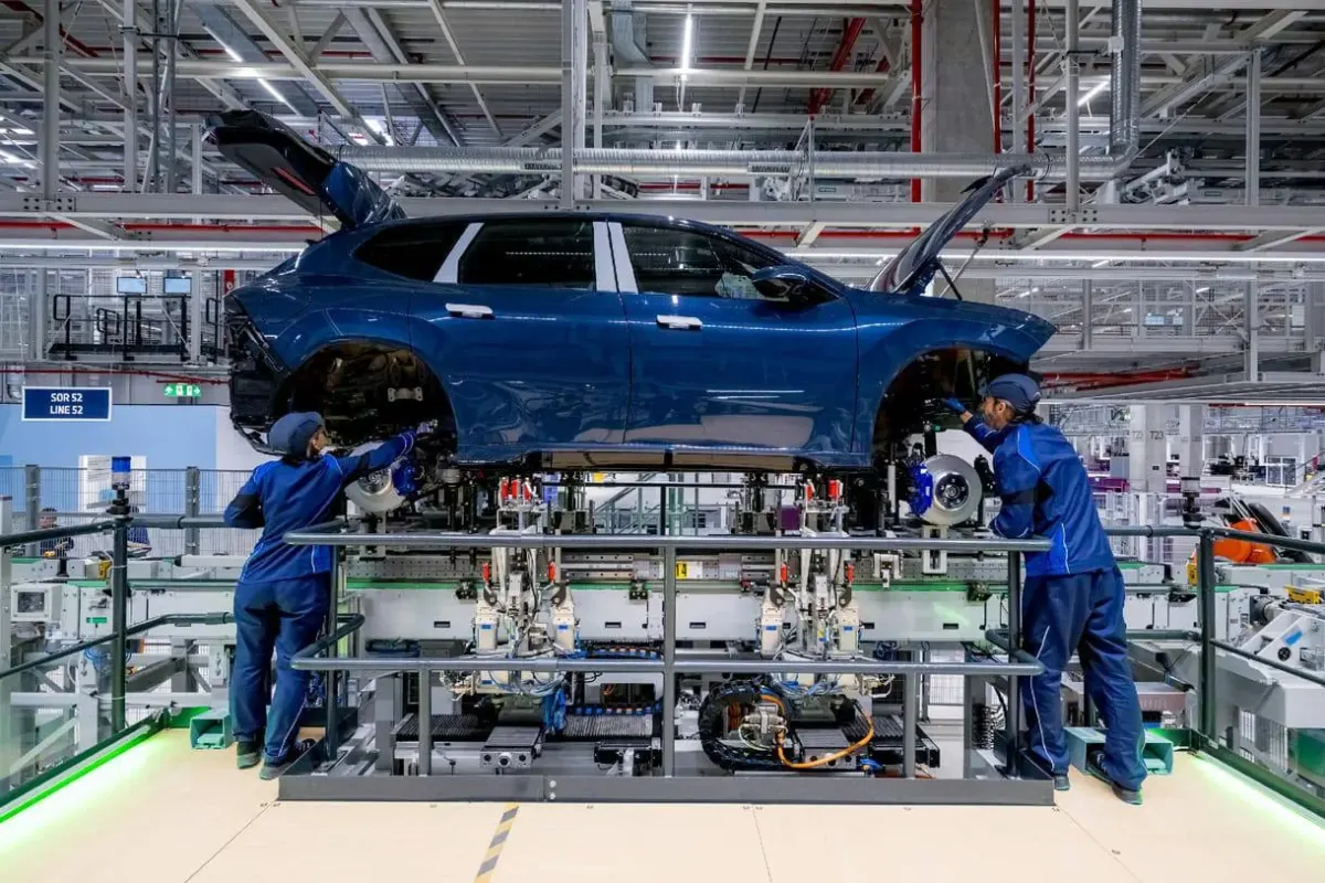 Blue sedan on a factory assembly line with technicians working nearby